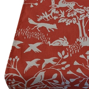 May include: Red fabric with a white pattern of stylised animals and plants. The pattern includes a fox, a rabbit, birds, and trees.