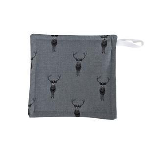 Puede incluir: Un cuadrado gris para agarrar ollas con un patrón repetido de ciervos negros. Tiene un lazo blanco para colgar. Los ciervos están representados con grandes astas y están de pie sobre la tela.