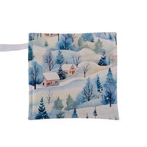 Puede incluir: Bolsa de tela cuadrada con un estampado de paisaje invernal. El diseño presenta colinas cubiertas de nieve, árboles de hoja perenne y pequeñas casas con detalles en rojo. Un lazo blanco está unido en la esquina superior izquierda.