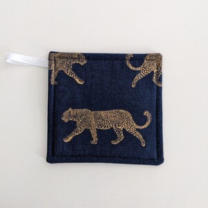 May include: A blue pot holder with a white hanging loop features a repeating pattern of gold leopard silhouettes.