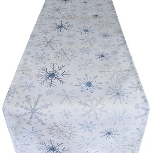 May include: A white table runner with a blue snowflake pattern. The snowflakes are of varying sizes and are scattered across the runner.