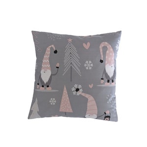 Peut inclure: Un coussin carré décoratif avec un fond gris présentant un motif répété de gnomes, d'arbres de Noël, de flocons de neige et de cœurs. Les gnomes portent des chapeaux roses et blancs et ont des barbes blanches. Les arbres et les flocons de neige sont blancs.