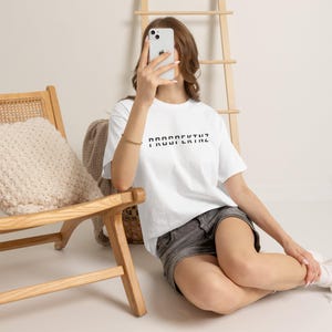 Può includere: Una t-shirt bianca a maniche corte con il testo nero PROSPEKTNZ stampato sul petto. La maglietta è abbinata a pantaloncini di jeans grigio scuro. Il design è semplice e pulito, concentrandosi sulla scritta in grassetto sul davanti del capo.