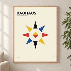 Op de afbeelding: Een ingelijste poster met een crèmekleurige achtergrond met de zwarte tekst BAUHAUS en STRAHL FORM ZENTRUM bovenaan, DESSAU en 1927 onderaan, en een centraal geometrisch sterontwerp bestaande uit zwarte, gele, blauwe en rode driehoeken.
