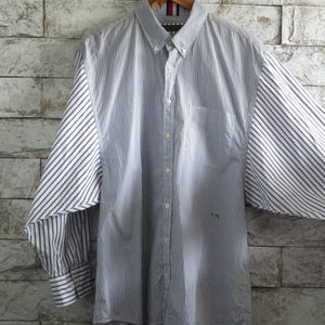 May include: A button-down shirt with vertical blue and white stripes on the front and back, and diagonal stripes on the sleeves. The shirt has a button-down collar and a small pocket on the chest.