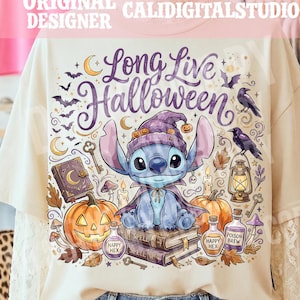 May include: A cream-colored t-shirt featuring a graphic of a blue alien character wearing a purple witch hat and cape, sitting on spell books. The design includes pumpkins, a lantern, ravens, bats, and text that reads Long Live Halloween.