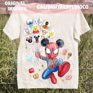 May include: A cream-colored t-shirt featuring a graphic of a character wearing a red and blue spider-themed suit with mouse ears, holding a cluster of balloons containing various cartoon characters, surrounded by small icons of snacks and stars.