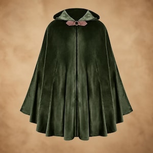 May include: A dark forest green velvet hooded cloak featuring a pleated design and a metallic ring closure at the neck. The interior of the hood is lined with a lighter sage green fabric, and the clasp is secured with dusty rose coloured fabric tabs.