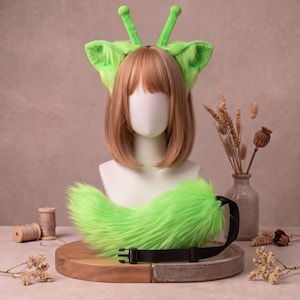 Puede incluir: Una diadema de piel sintética de color verde lima brillante con dos orejas puntiagudas y dos antenas con puntas redondeadas, junto con una cola de piel sintética a juego sujeta a una correa negra ajustable con hebilla de plástico.