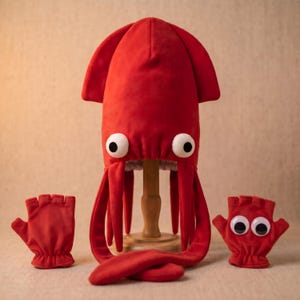May include: A bright red squid-shaped hat featuring two large white eyes with black pupils and long dangling tentacles. Accompanying the hat are two matching red fingerless gloves, each decorated with a pair of large white eyes with black pupils.