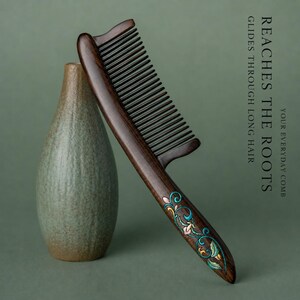 May include: A dark brown wooden comb with a long handle featuring an inlaid floral pattern in shades of teal, pink, and gold. The text on the right reads: REACHES THE ROOTS GLIDES THROUGH LONG HAIR YOUR EVERYDAY COMB.