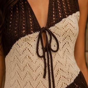 May include: A sleeveless knit top featuring a deep V-neckline with a dark brown tie closure. The garment displays a two-tone chevron pattern in dark brown and cream, constructed with an openwork stitch design throughout the bodice.
