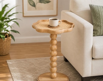 May include: A light brown side table with a flower-shaped top featuring a woven rattan surface. The table has a central pedestal base composed of stacked wooden spheres resting on a flat circular wooden base. A white mug sits on top.