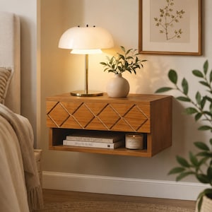 May include: A wall-mounted wooden nightstand featuring a single drawer with a diamond-patterned front. The unit includes an open storage shelf below holding two books titled Live Beautifully and This Is Home, plus a glass candle jar.