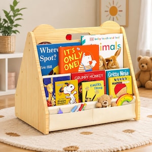 May include: A light-colored wooden bookshelf with bear-shaped side panels, filled with various children's books including Where's Spot, It's Only One, Grumpy Monkey, and Gritty Ninja. A fabric pocket at the front holds pens and a small teddy bear.