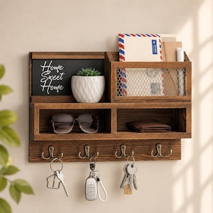 May include: A dark brown wooden wall organizer featuring a chalkboard with the text Home Sweet Home, a small white succulent planter, a wire mesh mail slot, two open storage compartments, and four metal hooks holding various sets of keys.