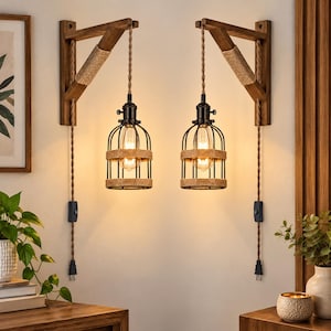 May include: A pair of wall-mounted lamps featuring wooden brackets wrapped in natural rope. Each lamp has a black metal cage shade accented with rope, a hanging cord with an inline switch, and a warm glowing light bulb inside the cage.