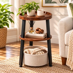 May include: A three-tier round side table with a dark wood finish and black metal legs. The top shelf holds a potted green plant and a white mug. The middle shelf features a glass reed diffuser, a wooden knot sculpture, and two stacked books.