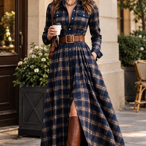 May include: A long-sleeved maxi shirt dress in a navy blue and tan plaid pattern. The dress features a button-down front, a collar, two chest pockets, and a wide brown leather belt with a gold buckle at the waist. The skirt has a front slit.