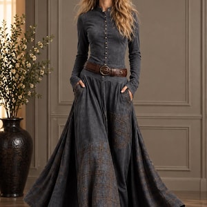 Puede incluir: Un vestido gris carbón de manga larga con corpiño abotonado, cinturón de cuero marrón en la cintura y falda larga con bolsillos integrados y paneles de tela a cuadros en tonos marrón y gris en el dobladillo y el lateral.