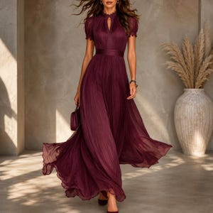Peut inclure: Une robe longue plissée de couleur bordeaux profond, dotée de manches courtes bouffantes, d'un col montant avec une ouverture en forme de goutte d'eau au centre et d'une taille ajustée. La jupe est en tissu léger et fluide.
