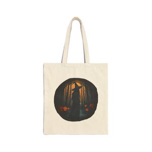 Peut inclure: Un sac fourre-tout en toile beige avec une impression graphique circulaire représentant une silhouette portant un chapeau pointu dans une forêt sombre. La scène inclut des citrouilles d'Halloween orange lumineuses parmi les arbres.