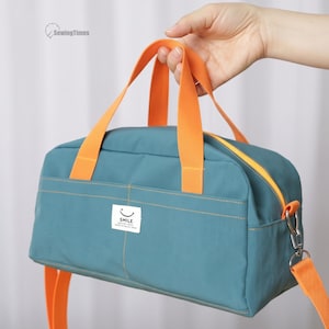 Può includere: Una borsa rettangolare color verde acqua con manici arancioni brillanti e una tracolla abbinata. La borsa presenta una tasca frontale con un'etichetta rettangolare bianca che riporta un'icona a forma di faccina sorridente e la scritta "SMILE".