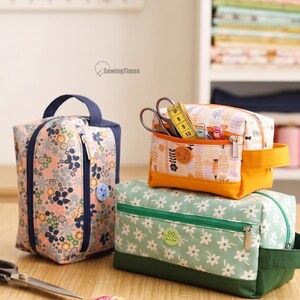 May include: Three fabric pouches for storage. One tall pouch with a floral pattern and blue handle, one small pouch with a yellow base and patterned top containing scissors and tape, and one long green pouch with white flowers.