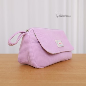 Peut inclure: Une pochette zippée en velours côtelé violet clair dotée d'un rabat avant avec une petite étiquette rectangulaire portant l'inscription SewingTimes. La pochette comprend une dragonne assortie fixée à la tirette de fermeture éclair.