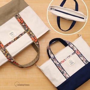 Può includere: Due borse tote in tela con pannelli color bianco sporco, finiture in tessuto floreale e basi in tinta unita verde oliva e blu navy. Ogni borsa include una piccola etichetta rettangolare con il disegno di un gatto e il testo "HAVE A NICE DAY".