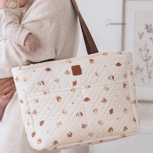 Op de afbeelding: Een crèmekleurige gewatteerde tas met een herhalend patroon van kleine bruine en beige hondengezichten. De tas heeft twee bruine schouderbanden, een rechthoekige bruine kunstlederen patch aan de voorzijde en twee buitenzakken. Tekst: SewingTimes.