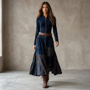 Könnte beinhalten: Ein langärmeliges, dunkelblaues Oberteil mit Knopfleiste und ein dazu passender Rock mit einem Patchwork-Muster aus Karos in Blau- und Brauntönen. Das Outfit wird durch einen breiten braunen Ledergürtel in der Taille und braune Stiefel ergänzt.