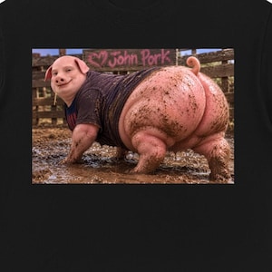 Op de afbeelding: Een zwart t-shirt met een grafische print van een varken met een menselijk gezicht dat een donker shirt draagt en in de modder staat. Het varken staat voor een houten hek met de tekst John Pork op een bordje met een hartje.