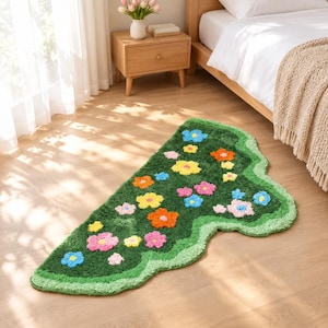May include: An irregularly shaped area rug featuring a deep green background with a wavy light green border. The rug is decorated with a scattered pattern of small, tufted flowers in vibrant shades of yellow, orange, pink, and light blue.