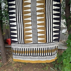 May include: A rectangular textile featuring a repeating pattern of vertical black and white stripes interspersed with columns of mustard yellow shapes. The lower section displays a horizontal border with intricate black and white leaf motifs.
