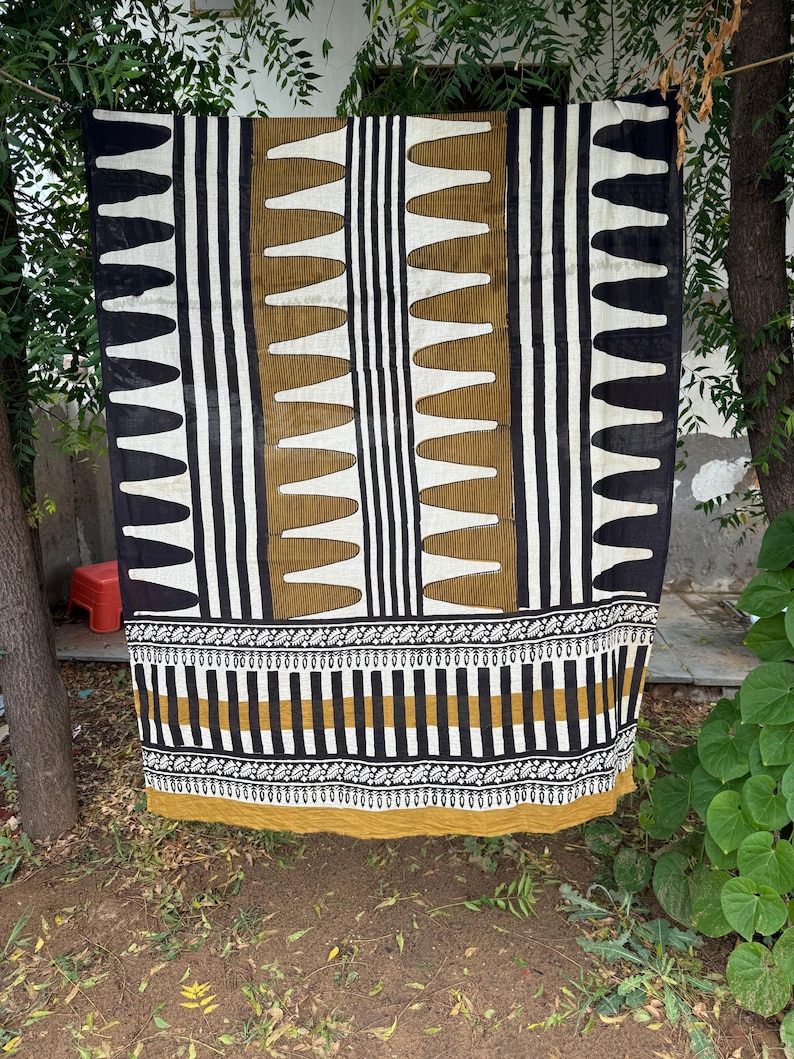 May include: A rectangular textile featuring a repeating pattern of vertical black and white stripes interspersed with columns of mustard yellow shapes. The lower section displays a horizontal border with intricate black and white leaf motifs.