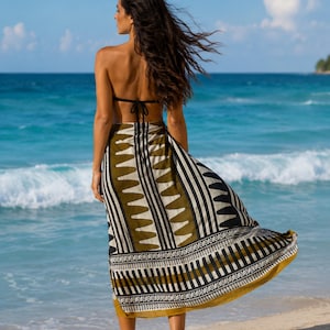 May include: A long sarong wrap skirt featuring a bold geometric pattern in olive green, black, and cream. The fabric displays alternating vertical stripes, triangular motifs, and intricate border details, flowing loosely around the lower body.
