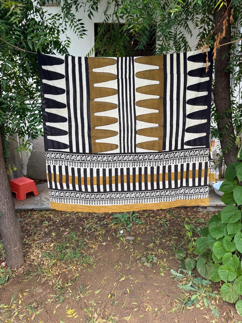 May include: A rectangular textile featuring a geometric pattern in black, white, and mustard yellow. The design includes vertical stripes, repeating pointed shapes, and a horizontal border with intricate floral motifs along the bottom edge.