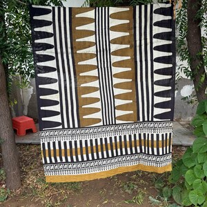 May include: A rectangular textile featuring a repeating pattern of black and white vertical stripes interspersed with columns of mustard yellow shapes. The lower section displays a horizontal border with intricate black, white, and yellow geometric motifs.