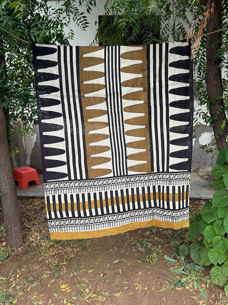May include: A rectangular textile featuring a repeating pattern of black and white vertical stripes interspersed with columns of mustard yellow shapes. The lower section displays a horizontal border with intricate black, white, and yellow geometric motifs.
