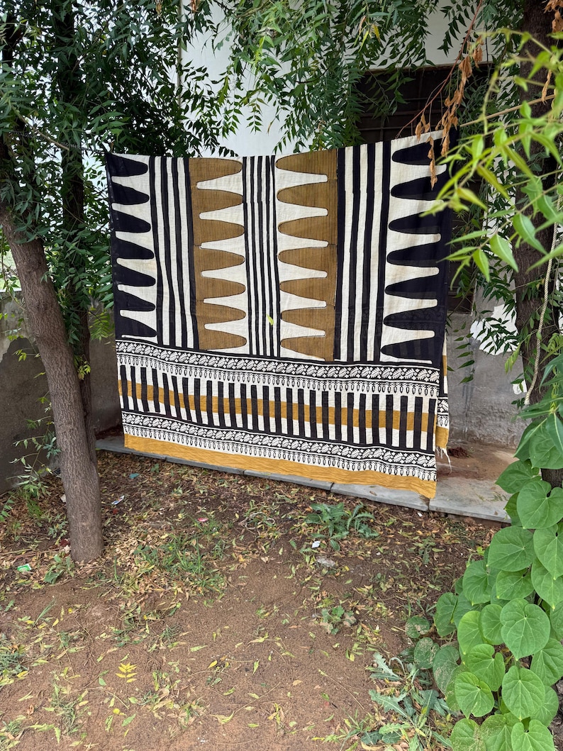 May include: A rectangular textile featuring a bold geometric pattern in black, white, and mustard yellow. The design includes vertical stripes, repeating triangular shapes, and a horizontal border with intricate floral motifs along the bottom edge.