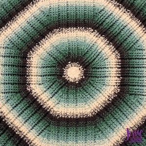 May include: A close-up of a crocheted circular blanket with a concentric pattern of white, teal, and black yarn.