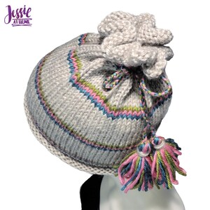 May include: A light grey knitted hat with a drawstring and a decorative tassel. The hat has colourful stripes in pink, blue, and green. The text "Jessie at Home" is in the upper left corner.
