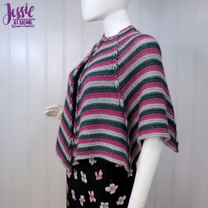 Può includere: Uno scialle a righe in tonalità rosa, verde e grigio con un bordo all'uncinetto. Lo scialle è drappeggiato su un manichino bianco.