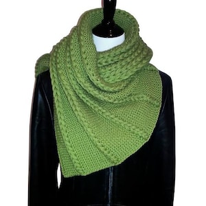 May include: A green knitted infinity scarf with a cable knit pattern. The scarf is draped over a black leather jacket.