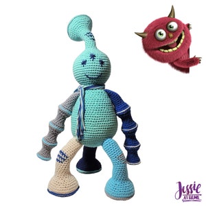 May include: A handmade crochet doll in shades of teal, blue, gray, and beige. The doll has a whimsical design with a long neck, a scarf, and a smiling face. A cartoon monster peeks in from the right side of the image.