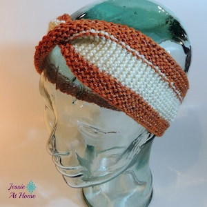 May include: A hand-knitted headband in shades of orange and cream. The headband features a twisted design with a central cream-colored stripe. The text "Jessie At Home" is visible in the lower left corner.