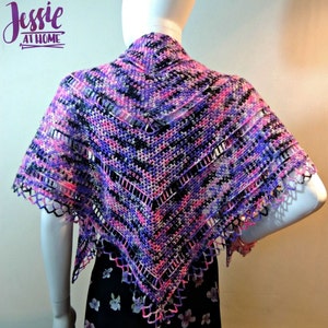 May include: A crocheted shawl in shades of pink, purple, and black with a lacy border. The shawl is draped over a mannequin's shoulders.