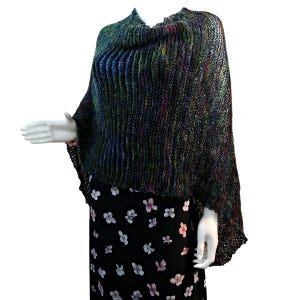 Può includere: Un poncho di maglia verde, blu e nero con collo a lupetto. Il poncho ha una vestibilità ampia ed è realizzato con un filato morbido e leggero.