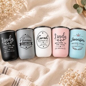 May include: Five cylindrical tumblers in black, grey, white, pink, and light blue, each featuring custom black text and graphics. The tumblers display names like Linda, Thomas, Sarah, and Jennifer, along with professional titles and team messages.